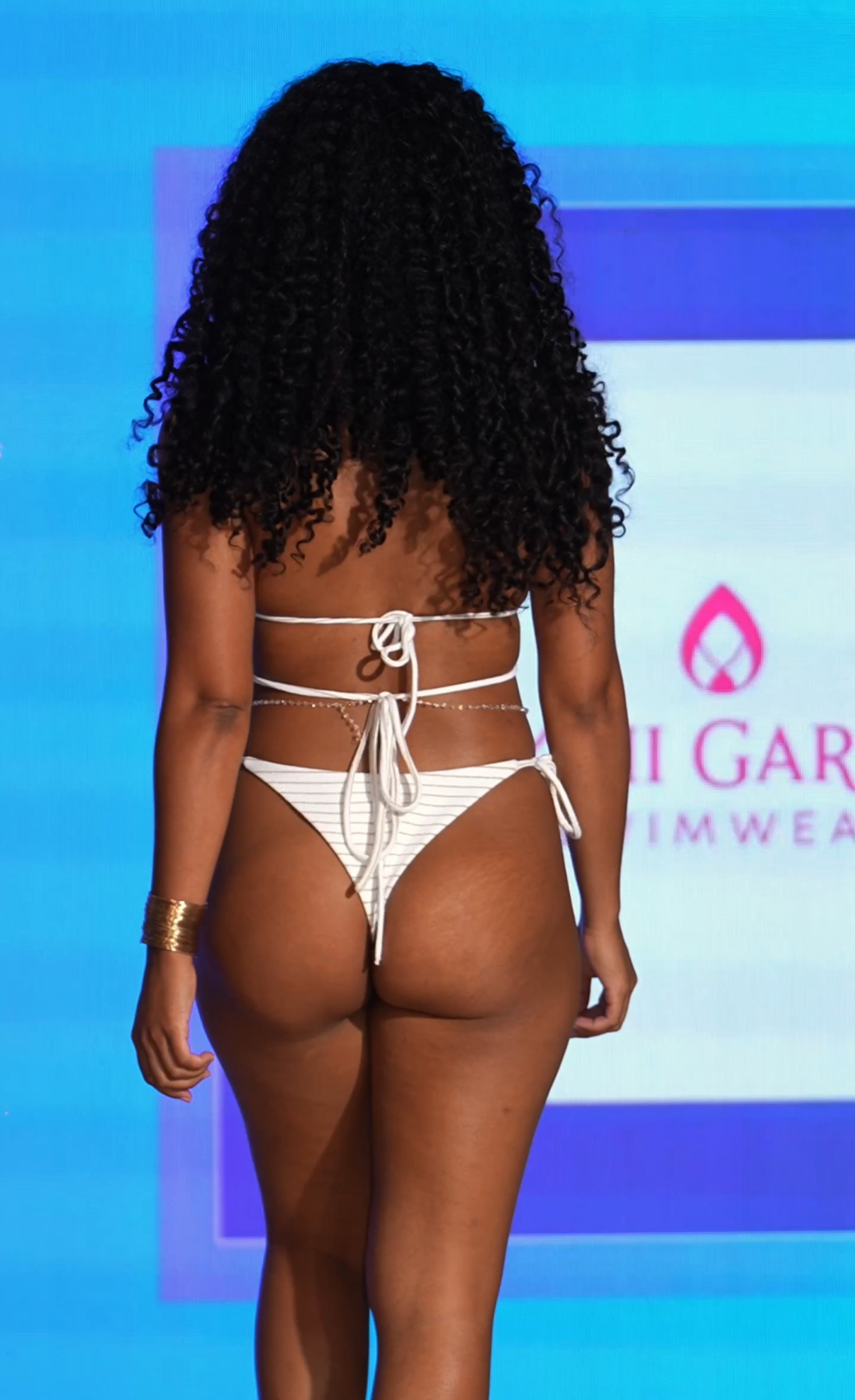 Person wearing a white bikini on a blue background with branding visible